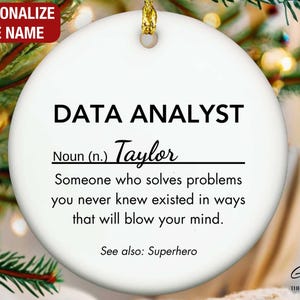 May include: A white ceramic Christmas ornament with gold string, featuring the text "DATA ANALYST" and a personalized name. The ornament includes a definition and the words "See also: Superhero."