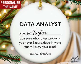 May include: A white ceramic Christmas ornament with gold string, featuring the text "DATA ANALYST" and a personalized name. The ornament includes a definition and the words "See also: Superhero."