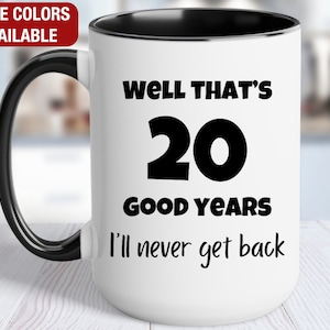 May include: White ceramic coffee mug with a black handle and black rim. The mug has black text that reads "Well that's 20 good years I'll never get back."