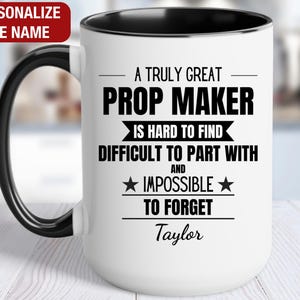 May include: White ceramic coffee mug with a black rim and handle. The mug has black text that reads "A truly great Prop Maker is hard to find, difficult to part with and impossible to forget." The name "Taylor" is printed below the text.