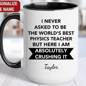 May include: White coffee mug with a black rim and handle. The mug has black text that reads "I never asked to be the world's best physics teacher but here I am absolutely crushing it." The name "Taylor" is printed below the text.