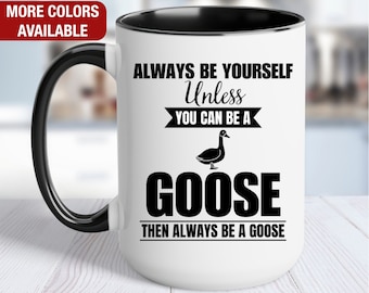 May include: White ceramic coffee mug with a black handle and black rim. The mug has a black and white graphic that says "Always be yourself unless you can be a goose then always be a goose".