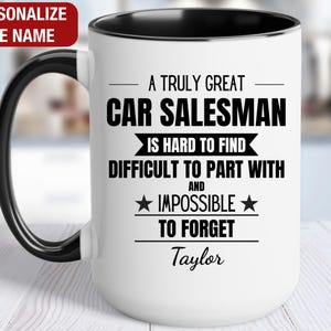 May include: White ceramic coffee mug with a black rim and handle. The mug features a black and white design that reads "A truly great car salesman is hard to find, difficult to part with and impossible to forget." The name "Taylor" is printed below the text.