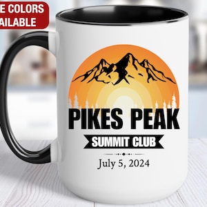 May include: White ceramic mug with a black rim and handle. The mug features a graphic of a mountain range with a sunset behind it. The text "Pikes Peak Summit Club" and "July 5, 2024" is printed on the mug.