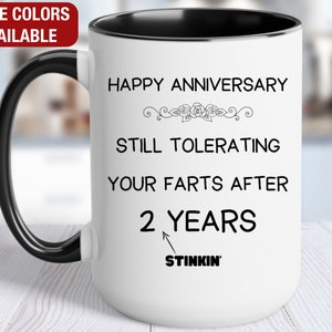May include: White ceramic coffee mug with a black rim and handle. The mug has black text that reads "Happy Anniversary Still Tolerating Your Farts After 2 Years Stinkin'"