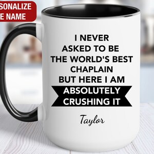 May include: White coffee mug with a black rim and handle. The mug has black text that reads "I never asked to be the world's best chaplain but here I am absolutely crushing it". The name "Taylor" is written in cursive below the text.