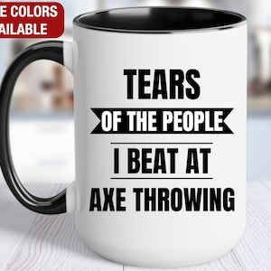 May include: White ceramic coffee mug with a black handle and black rim. The mug has black text that reads "Tears of the People I Beat at Axe Throwing."