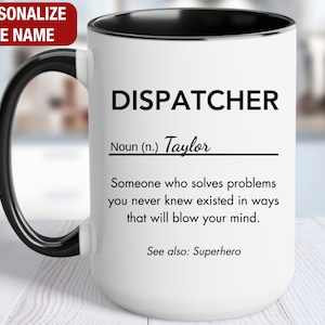 May include: White ceramic mug with a black handle and rim. The mug has a black and white design that reads "DISPATCHER Noun (n.) Taylor Someone who solves problems you never knew existed in ways that will blow your mind. See also: Superhero"