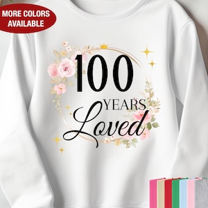 May include: White sweatshirt featuring a floral design and the text "100 Years Loved" in black.