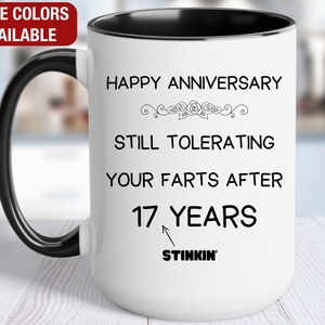 May include: White ceramic coffee mug with a black handle and black rim. The mug has a funny anniversary message that reads "Happy Anniversary Still Tolerating Your Farts After 17 Years Stinkin'"