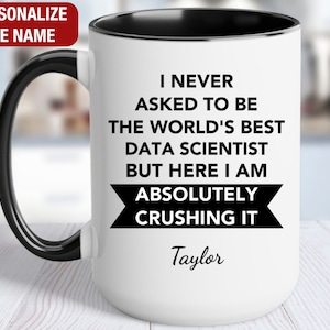 May include: White ceramic mug with a black rim and handle. The mug has black text that reads "I never asked to be the world's best data scientist but here I am absolutely crushing it." The name "Taylor" is written in cursive below the text.