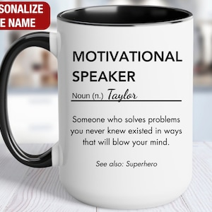 May include: White ceramic coffee mug with a black handle and black rim. The mug has a black and white design that reads "Motivational Speaker Noun (n.) Taylor Someone who solves problems you never knew existed in ways that will blow your mind. See also: Superhero"