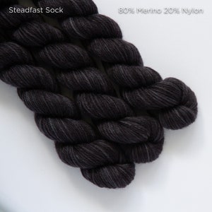Può includere: Un gomitolo di filato grigio scuro etichettato "Steadfast Sock 80% Merino 20% Nylon".