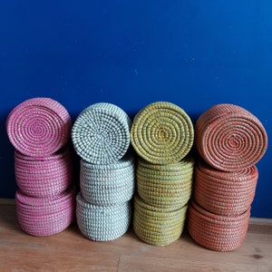 May include: Set of six woven storage baskets in pink, white and yellow. The baskets are stacked in three pairs, with the top layer featuring a round, woven lid.