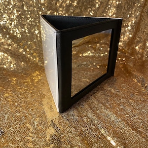 May include: A black and white triangular makeup mirror with a hinged lid. The mirror is closed and the lid is facing the camera.