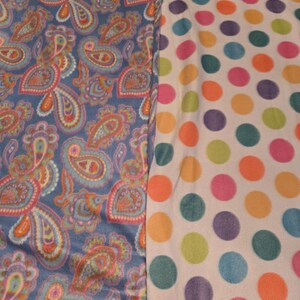 K&ouml;nnte beinhalten: Zwei Stoffmuster werden gezeigt. Eines ist ein blaues Paisley-Design mit orangefarbenen, rosa und t&uuml;rkisfarbenen Akzenten. Das andere ist ein wei&szlig;er Stoff mit gro&szlig;en, farbenfrohen Tupfen in Orange, Gr&uuml;n, Lila und Rosa.