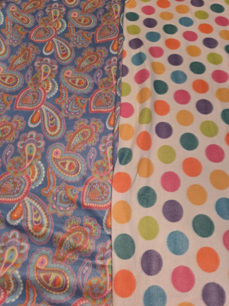 K&ouml;nnte beinhalten: Zwei Stoffmuster werden gezeigt. Eines ist ein blaues Paisley-Design mit orangefarbenen, rosa und t&uuml;rkisfarbenen Akzenten. Das andere ist ein wei&szlig;er Stoff mit gro&szlig;en, farbenfrohen Tupfen in Orange, Gr&uuml;n, Lila und Rosa.