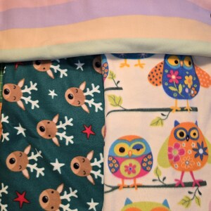 K&ouml;nnte beinhalten: Ein Stapel Fleece-Decken mit verschiedenen Mustern. Eine Decke hat pastellfarbene horizontale Streifen. Eine andere zeigt Rentiere und Schneeflocken auf teal-farbenem Hintergrund. Die dritte Decke zeigt bunte Eulen auf &Auml;sten vor wei&szlig;em Hintergrund.