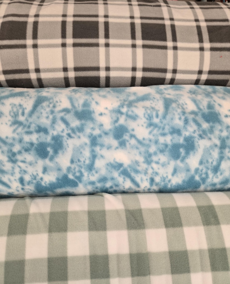 K&ouml;nnte beinhalten: Drei Rollen aus Fleece-Stoff. Die obere Rolle hat ein schwarz-wei&szlig;-graues Karomuster. Die mittlere Rolle hat ein blau-wei&szlig;es Spritzmuster. Die untere Rolle zeigt ein wei&szlig;-gr&uuml;nes Vichy-Muster.