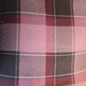 K&ouml;nnte beinhalten: Nahaufnahme einer weichen, karierten Decke. Die Decke weist ein Muster aus sich kreuzenden Linien in Rosa-, Grau- und Burgundert&ouml;nen mit d&uuml;nnen wei&szlig;en Linien auf. Der Stoff scheint aus Fleece zu sein.