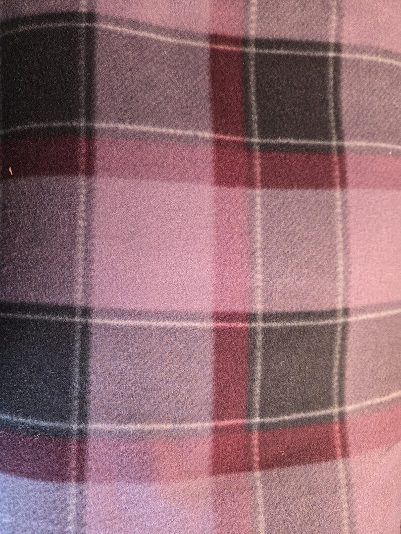 K&ouml;nnte beinhalten: Nahaufnahme einer weichen, karierten Decke. Die Decke weist ein Muster aus sich kreuzenden Linien in Rosa-, Grau- und Burgundert&ouml;nen mit d&uuml;nnen wei&szlig;en Linien auf. Der Stoff scheint aus Fleece zu sein.
