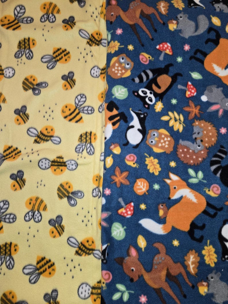 K&ouml;nnte beinhalten: Zwei Fleece-Stoffe mit unterschiedlichen Mustern. Einer ist gelb mit l&auml;chelnden Bienen. Der andere ist blau mit Waldtieren wie F&uuml;chsen, Rehen, Eulen und Waschb&auml;ren. Die Stoffe sind wahrscheinlich f&uuml;r Decken oder andere Textilprojekte.