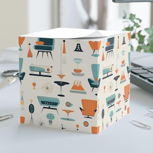 May include: A white cube-shaped notepad with a repeating pattern of mid-century modern furniture and decor in shades of orange, blue, and green.