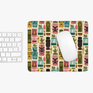 May include: A rectangular mousepad with a repeating pattern of colorful tiki masks, plants, and pots in shades of pink, teal, yellow, and brown. A white computer mouse rests on the pad, with a white keyboard in the background.