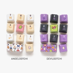 May include: A collection of custom keycaps, featuring the "ANGELGOTCHI" and "DEVILGOTCHI" themes. The keycaps are in various colors, with numbers and character designs. The "ANGELGOTCHI" set has a white, beige, and pink color scheme, while the "DEVILGOTCHI" set has a black and purple color scheme.