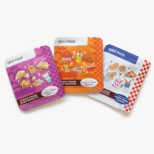 May include: Three food-themed acrylic charm blind booster packs. The packs are labelled "Taco Pack", "Jolli Pack", and "Kirk Pack". Each pack features illustrations of food items and the text "Add to your Fillable Shaker Keychain".
