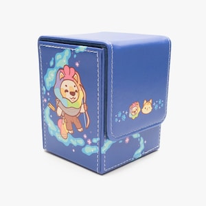 May include: A blue, square card storage box with a hinged lid. The box features a cartoon lion with a rainbow mane and bow and arrow on the front. Additional cartoon lion and cat graphics are on the lid. White stitching outlines the edges.