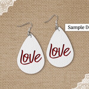 May include: White teardrop earrings with the word "love" in red script. The earrings have silver-colored hooks and are displayed on a textured, tan background. The text "Sample Design" is in a white rectangle.