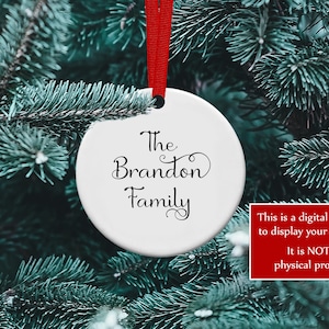 K&ouml;nnte beinhalten: Ein wei&szlig;er, runder Weihnachtsschmuck mit den Worten "The Brandon Family" in eleganter schwarzer Schrift, der an einem roten Band vor dem Hintergrund eines gr&uuml;nen Weihnachtsbaums h&auml;ngt. Ein rotes Feld in der Ecke besagt: "This is a digital mockup to display your designs. It is NOT a physical product."