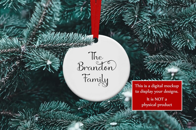 K&ouml;nnte beinhalten: Ein wei&szlig;er, runder Weihnachtsschmuck mit den Worten "The Brandon Family" in eleganter schwarzer Schrift, der an einem roten Band vor dem Hintergrund eines gr&uuml;nen Weihnachtsbaums h&auml;ngt. Ein rotes Feld in der Ecke besagt: "This is a digital mockup to display your designs. It is NOT a physical product."