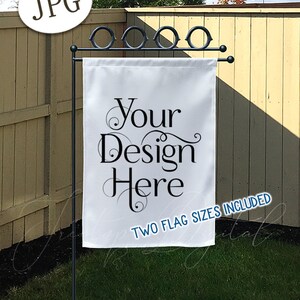 May include: A white garden flag mockup with the text "Your Design Here" in elegant script. The flag is displayed on a black metal stand with a decorative top, set against a backdrop of a wooden fence and green grass. The image includes the text "TWO FLAG SIZES INCLUDED".