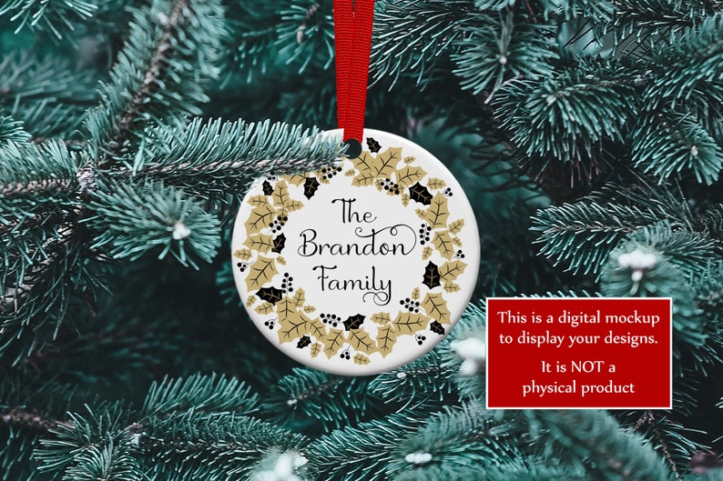 K&ouml;nnte beinhalten: Ein wei&szlig;er Keramik-Weihnachtsschmuck mit rotem Band, mit dem Text "The Brandon Family", umgeben von einem goldenen und schwarzen Stechpalmenkranz. Der Schmuck wird an einem Weihnachtsbaum pr&auml;sentiert.