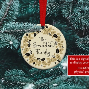 K&ouml;nnte beinhalten: Ein runder Weihnachtsschmuck mit rotem Band, mit dem Text "The Brandon Family", umgeben von einem Kranz aus goldenen Bl&auml;ttern und schwarzen Beeren. Der Schmuck h&auml;ngt vor gr&uuml;nem Tannennadel-Hintergrund.