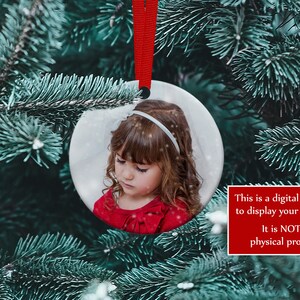K&ouml;nnte beinhalten: Ein runder Weihnachtsschmuck mit einem Foto eines Kindes, das an einem roten Band h&auml;ngt. Der Schmuck befindet sich vor dem Hintergrund eines Weihnachtsbaums. Der Text auf dem Bild lautet: "Dies ist ein digitales Mockup, um Ihre Designs anzuzeigen. Es ist KEIN physisches Produkt."