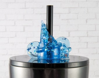 May include: A blue resin bottle stopper featuring a wizard hat and two circular accents, all filled with blue glitter and star-shaped confetti. The stopper sits atop a stainless steel container with a black stem.