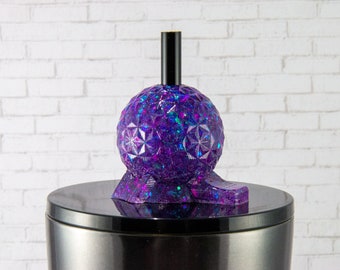 May include: Purple and blue glitter resin bottle stopper with a geometric design. The stopper has a black top and is sitting on a silver surface.