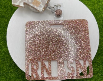 May include: A pink glitter badge holder with the text "RN BSN" cut out. The badge holder is attached to a retractable badge reel with a pink glitter charm.