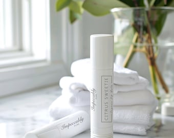 Könnte beinhalten: Zwei weiße Lippenbalsam-Tuben mit schwarzem Text. Die Tube links trägt die Aufschrift "Impeccably Pure". Die Tube rechts trägt die Aufschrift "Citrus Sweetie Organic Lip Balm Impeccably Pure".