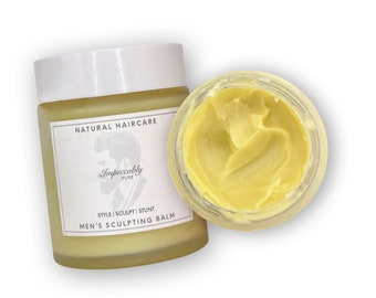 Könnte beinhalten: Ein klares Glas mit einem gelben Balsam darin. Das Glas hat ein weißes Etikett mit dem Text "Natural Haircare Impeccably Pure Style | Sculpt | Stunt Men's Sculpting Balm".