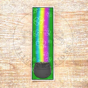 May include: A rectangular bookmark featuring a vertical rainbow gradient background transitioning from green to yellow to purple. The design includes white line art of multiple four-leaf clovers and a black pot filled with gold coins at the base.