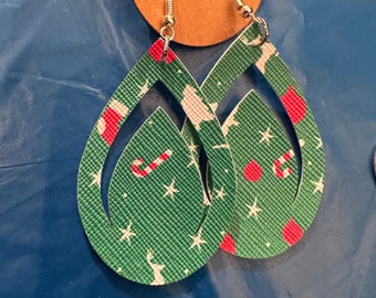 Puede incluir: Un par de pendientes colgantes de Navidad verdes con un patrón de estrella blanca y bastón de caramelo rojo. Los pendientes están hechos de cuero y tienen un gancho dorado.