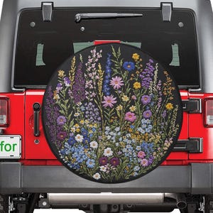Puede incluir: Un Jeep Wrangler rojo con una rueda de repuesto que presenta un diseño floral. La cubierta de la rueda es negra con un patrón floral colorido.