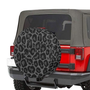 Könnte beinhalten: Ein roter Jeep mit einer schwarzen und grauen Leopardenmuster-Reserveradabdeckung. Der Jeep hat ein schwarzes Verdeck und eine schwarze Stoßstange hinten.