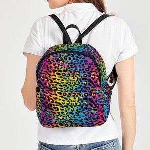 May include: A rainbow leopard print backpack with black straps. The backpack is small and has a rounded shape.