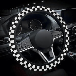 Pode incluir: Uma capa de volante xadrez em preto e branco instalada no volante de um carro. A capa tem um padrão repetido de quadrados pretos e brancos. O painel do carro e outros componentes internos são visíveis no fundo.