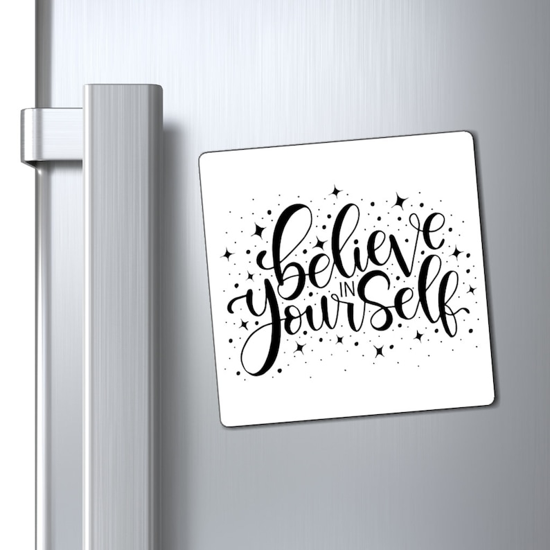 May include: White square refrigerator magnet with black lettering that reads "Believe in Yourself" with small black stars scattered around the text.